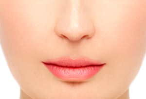 Nahaufnahme eines weiblichen Gesichts mit Fokus auf die rosafarbenen Lippen und glatte Haut. Die Lippen sind dezent geschminkt, die Haut ist ebenmäßig und gepflegt.