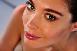 Nahaufnahme einer Frau mit strahlender Haut und leichtem Make-up, die in die Kamera lächelt.